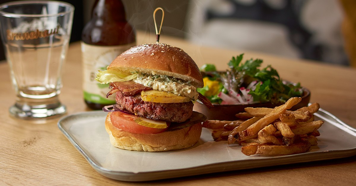 Burger de restaurant servi avec des frites et une salade, photographié en lumière naturelle chaleureuse.