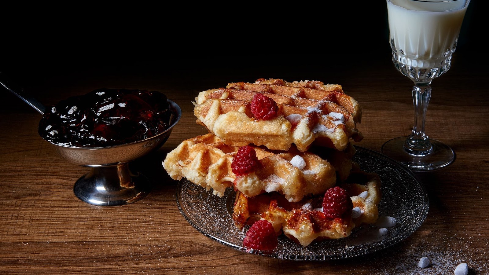 Gaufres de Liège empilées avec framboises et sucre, accompagnées de confiture et d'un verre de lait.