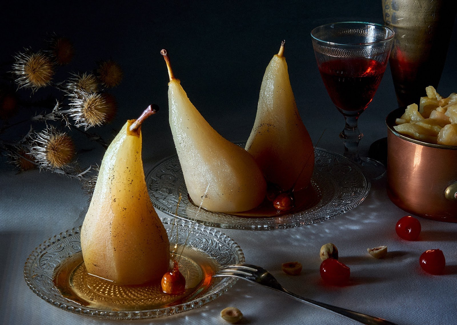 Poires pochées dressées sur des assiettes en verre, accompagnées de fruits rouges et d'un verre de vin.