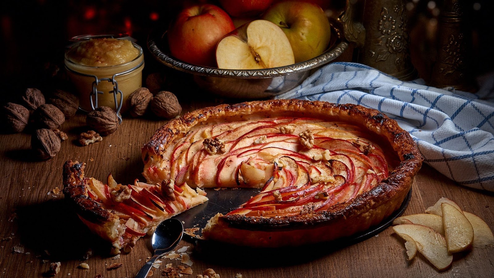 Tarte fine aux pommes et noix dans une mise en scène rustique en clair-obscur.